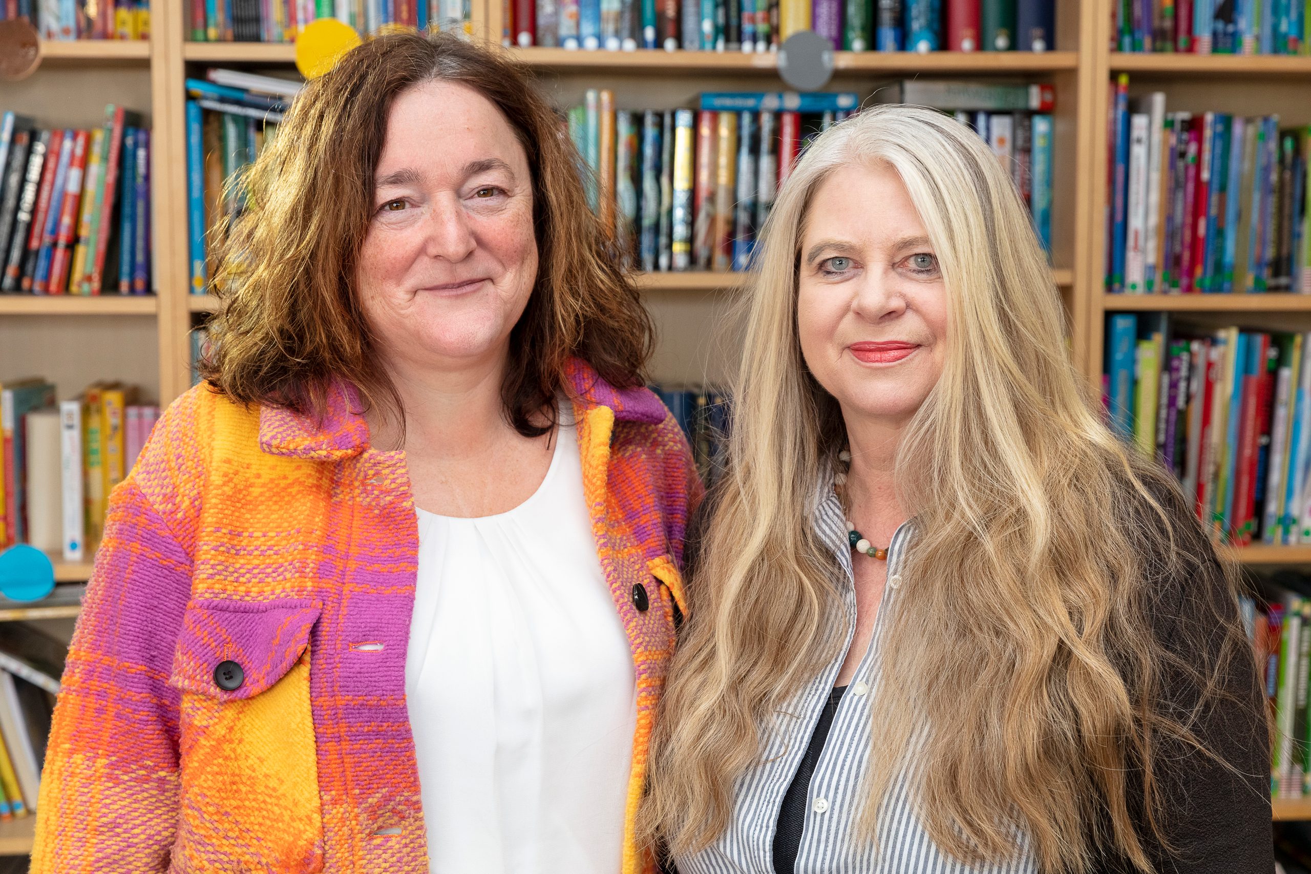 Schulter an Schulter stehen von links Schulleiterin Margeret Careddu-Bayr und Michaela Pelz vor einem Bücherregal.