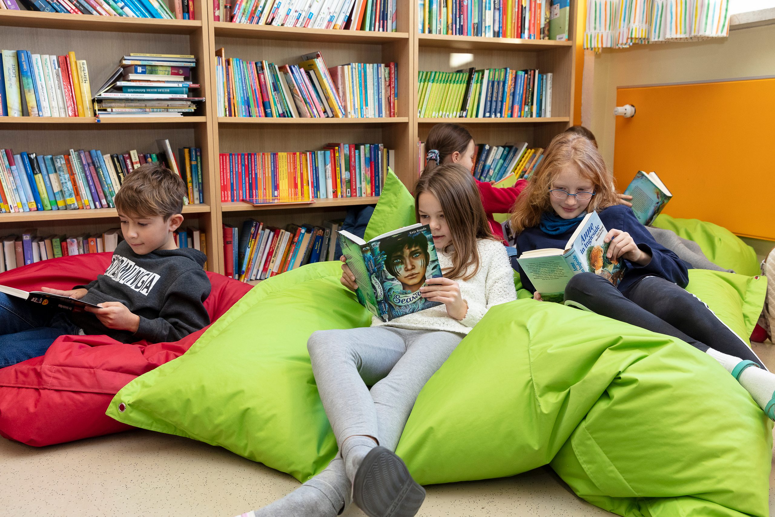 Kinder sitzen auf bunten Sitzsäcken und lesen in unterschiedlichen Büchern.
