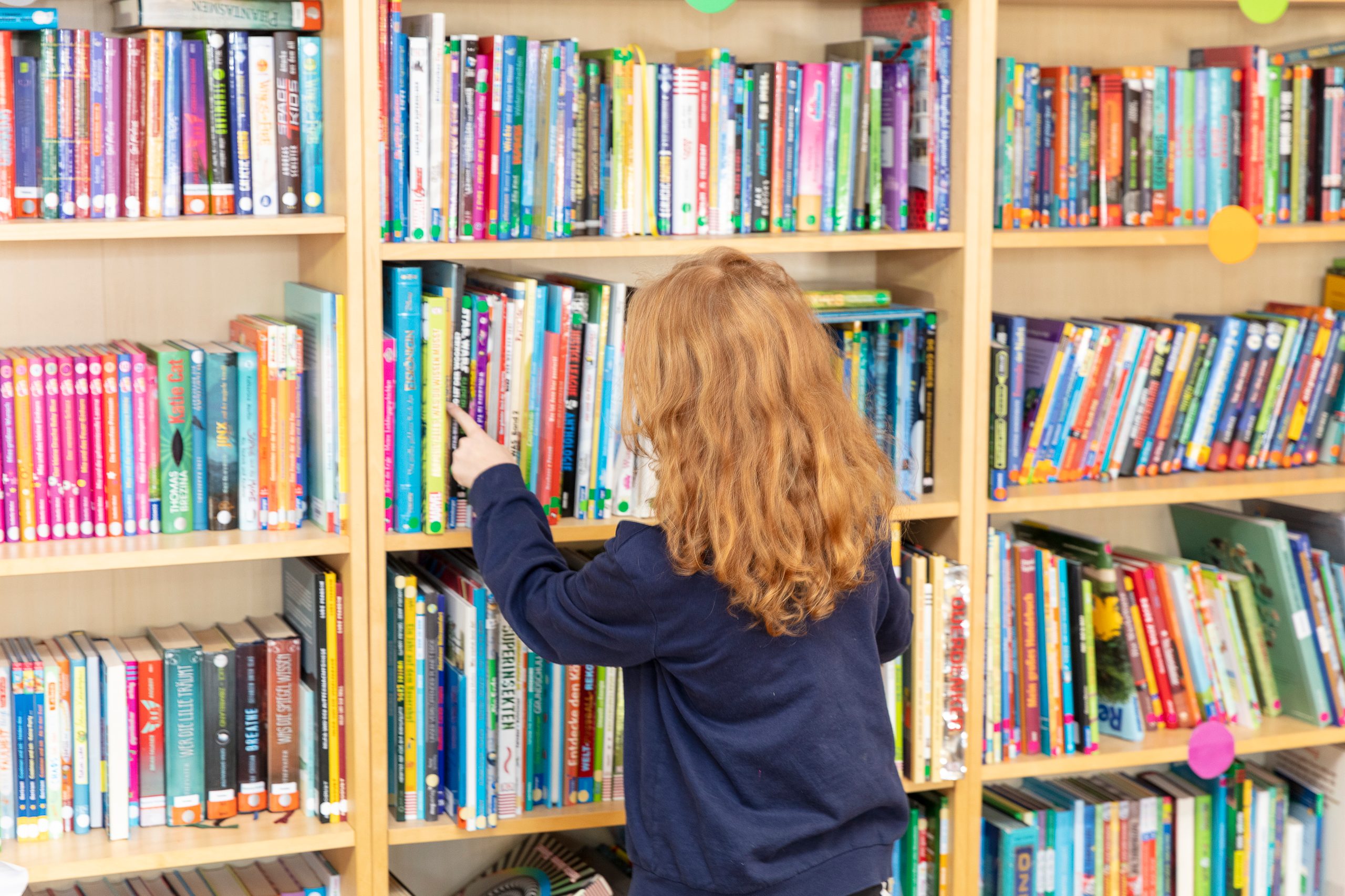 Anne steht vor einem großen Bücherregal und zählt Reihen und Bücher ab.