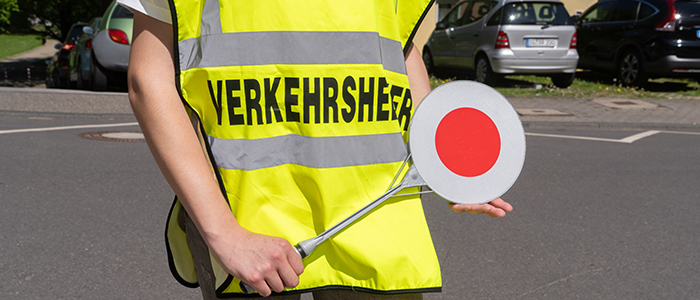 Eine Person mit Warnkelle in einer Weste mit Aufschrift "Verkehrshelfer"