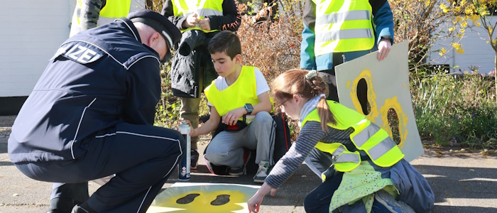 Kinder und ein Polizist tragen mit Schablone gelbe Markierung auf dem Boden auf