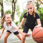 Zwei Mädchen in Sportkleidung spielen Basketball